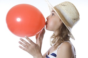 young girl blowing up a red balloon
