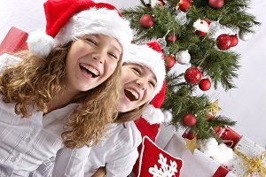 Two young girls laughing, wearing Santa hats in front of a Christmas tree