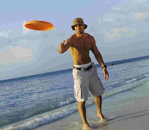 young man on beach wearing shorts throwing an orange colored frisbee