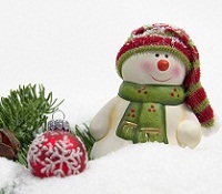 Snowman wearing a green scarf and striped hat standing next to a red christmas ornament