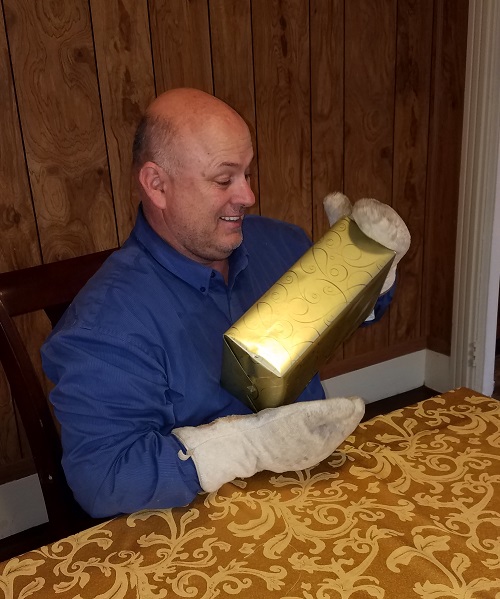 Happy man unwrapping a gift while wearing oven mitts.